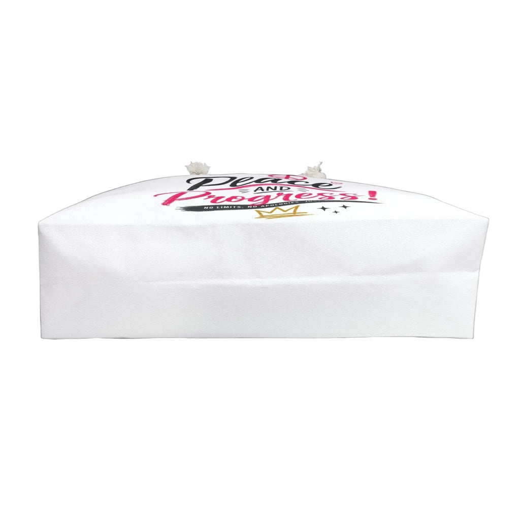 A white paper gift bag with a printed graphic on top featuring the words 'Grace and Progress!' in pink and black script, with a small gold crown and white ribbon ends, shown against a solid black background.