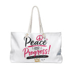 A white canvas tote bag with white rope handles, featuring a graphic print on the front that reads 'Peace and Progress!' in black and pink lettering, with a peace sign, small heart, and a gold crown.