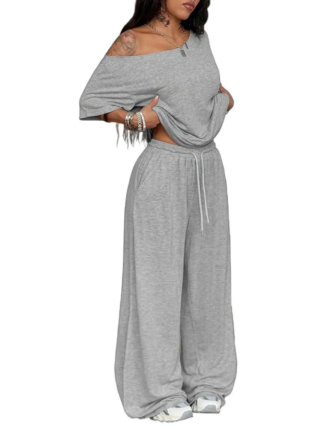 Woman wearing a gray off-shoulder top and wide-leg pants in a minimalistic room with black bean bags.
