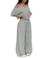 Woman wearing a gray off-shoulder top and wide-leg pants in a minimalistic room with black bean bags.