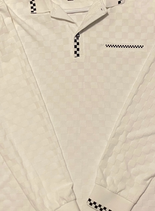 A white long-sleeve polo shirt with a subtle diamond quilted texture, featuring black and white checkered trim on the collar, placket, cuffs, and a small chest pocket detail. The shirt is laid flat on a textured concrete floor, hanging from a white plastic hanger.