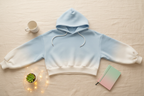Gradient blue-to-white oversized hoodie flat lay styled with mug, succulent, and journal on cream linen